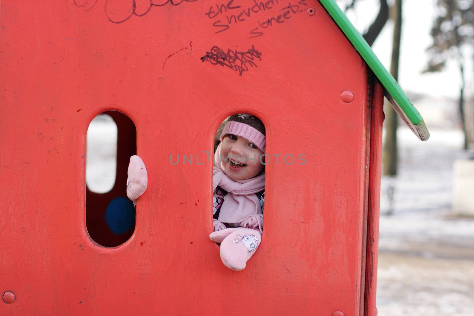 little happy girl play hide-and-seek at the kindergarten playground. Russian winter