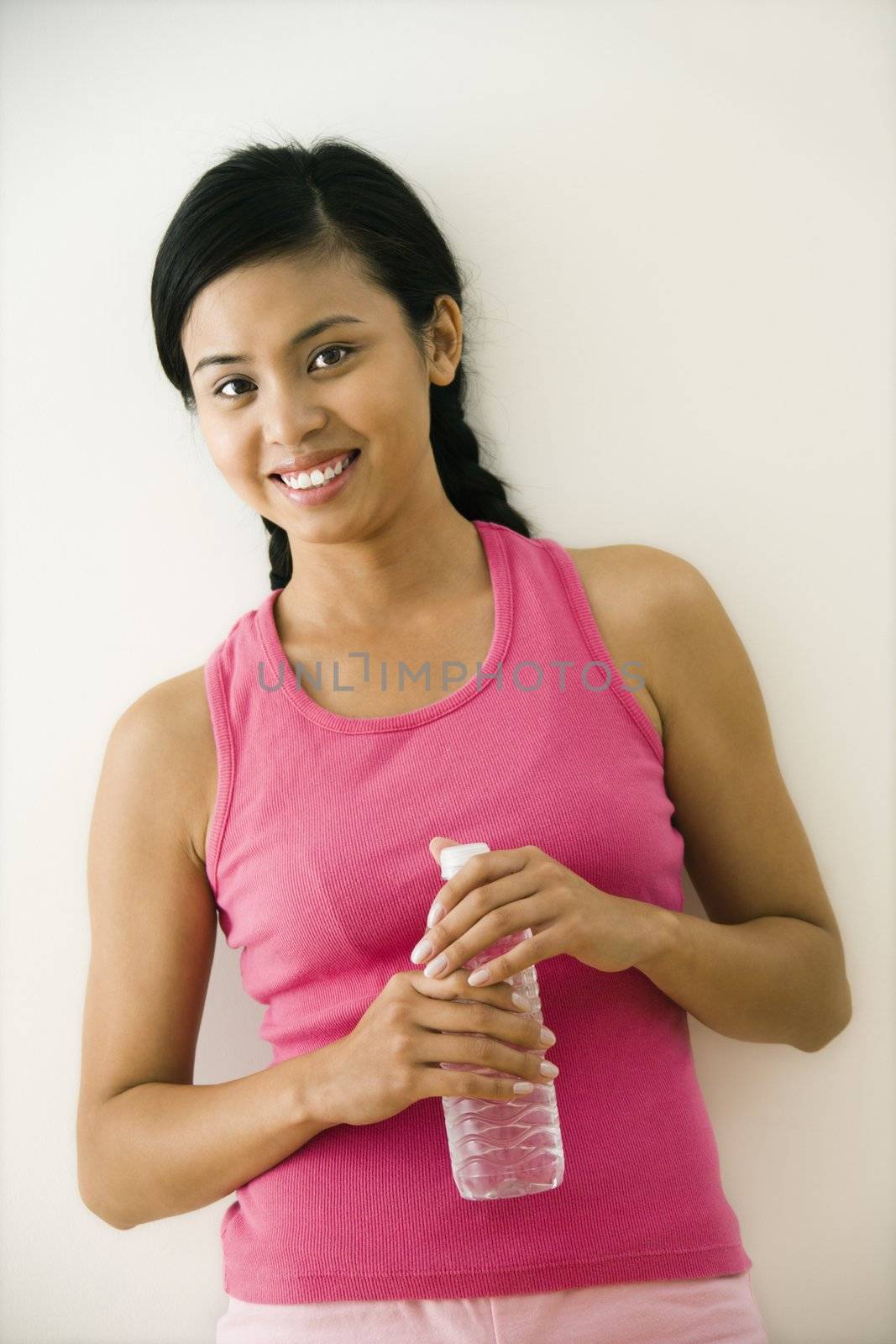 Portrait of smiling young Asian woman standing in fitness clothes holding bottle of water.