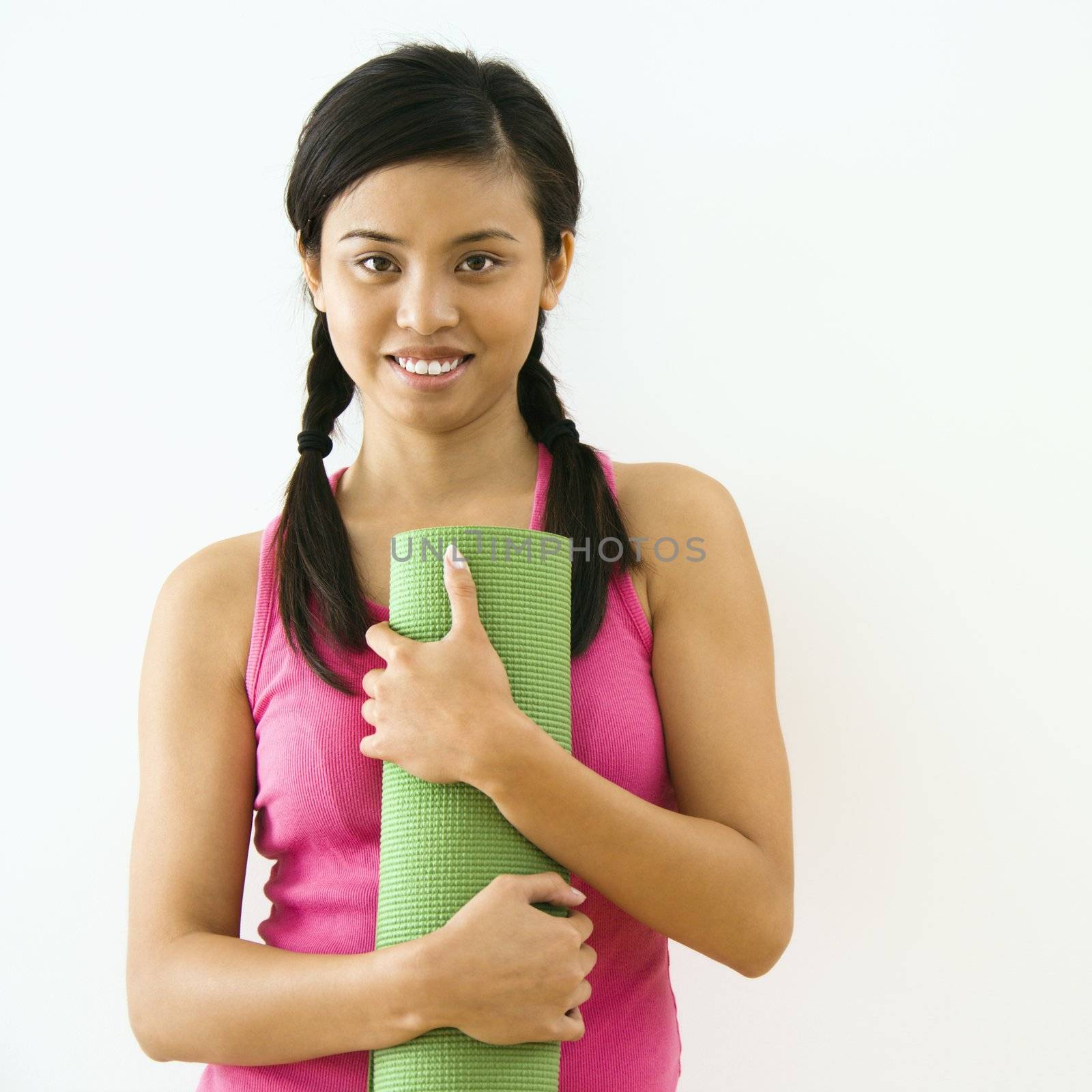 Portrait of smiling young Asian woman holding exercise mat.