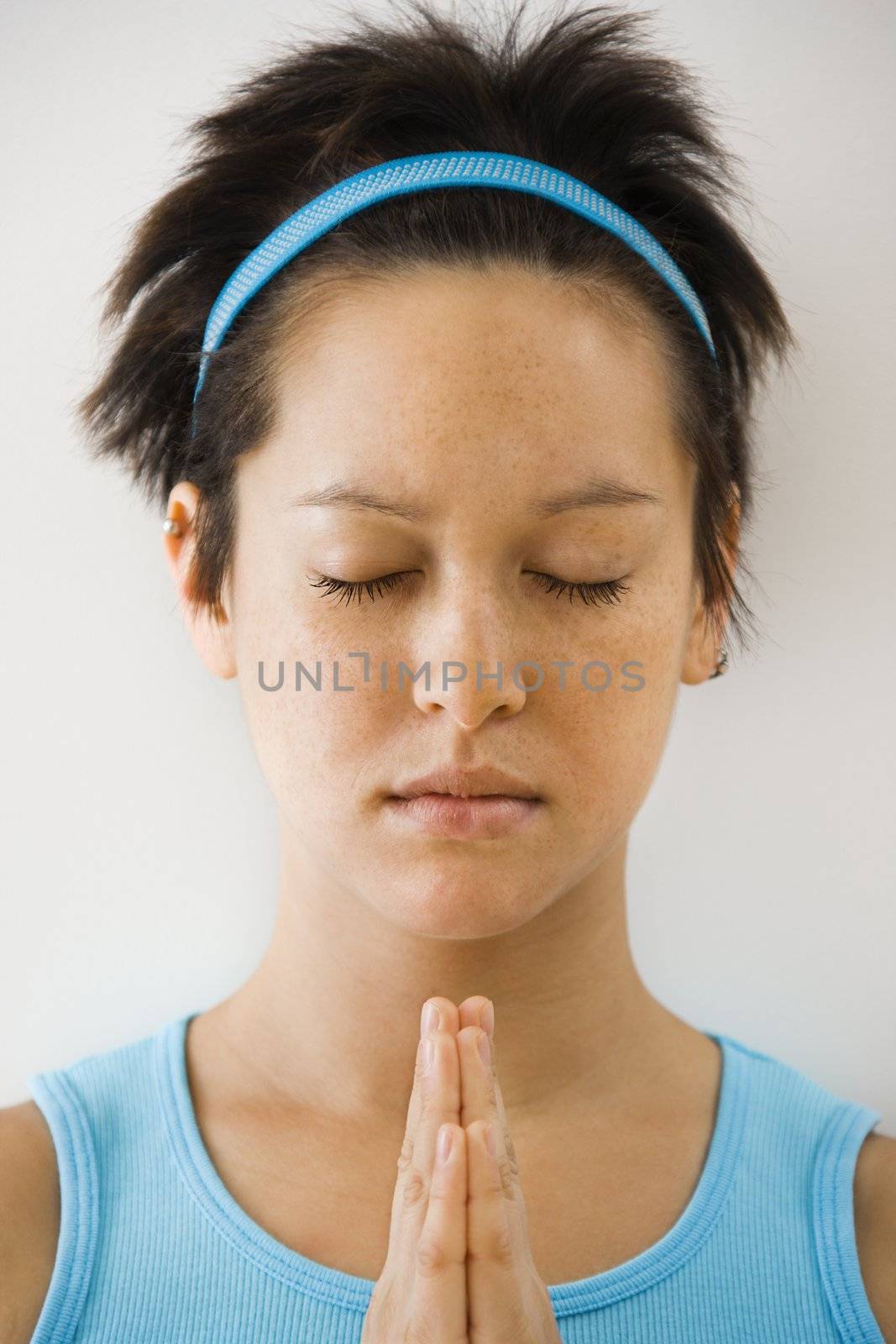 Young woman holding hands in prayer position with eyes closed meditating.