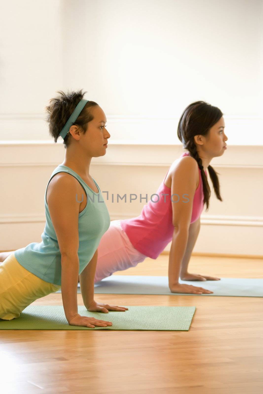 Two young women on yoga mats doing upward cobra pose.