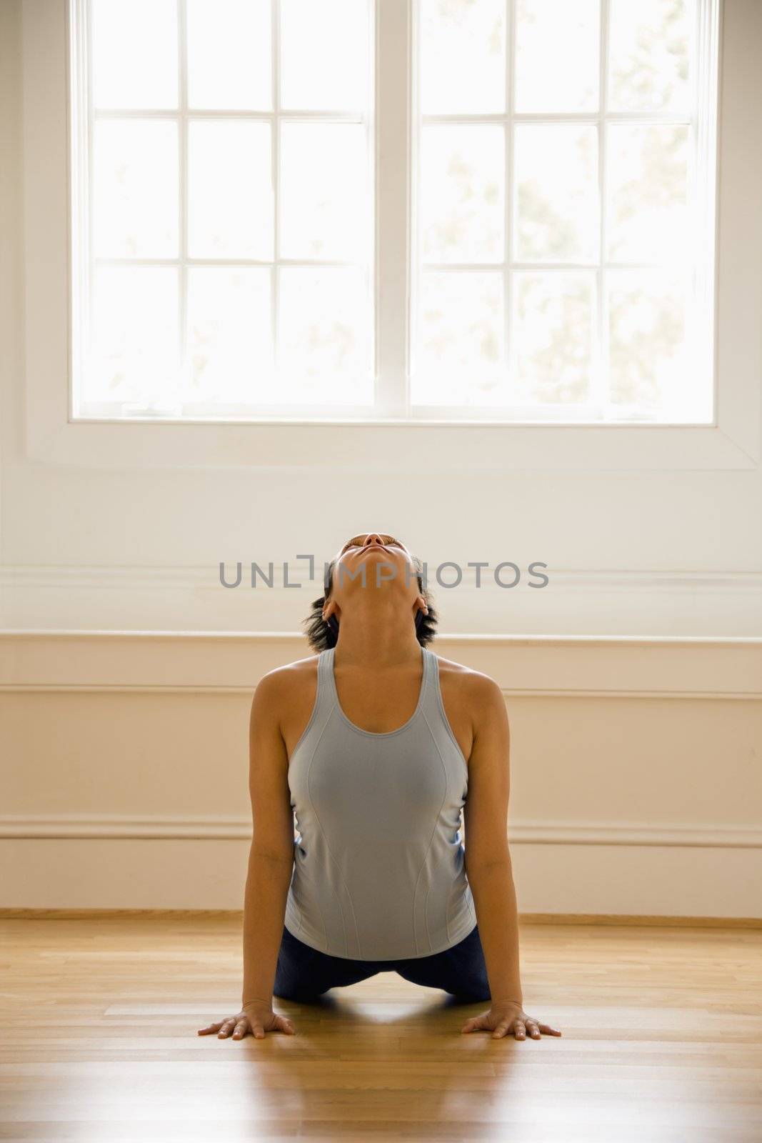 Young woman doing yoga cobra pose on wooden floor indoors by sunlit window.