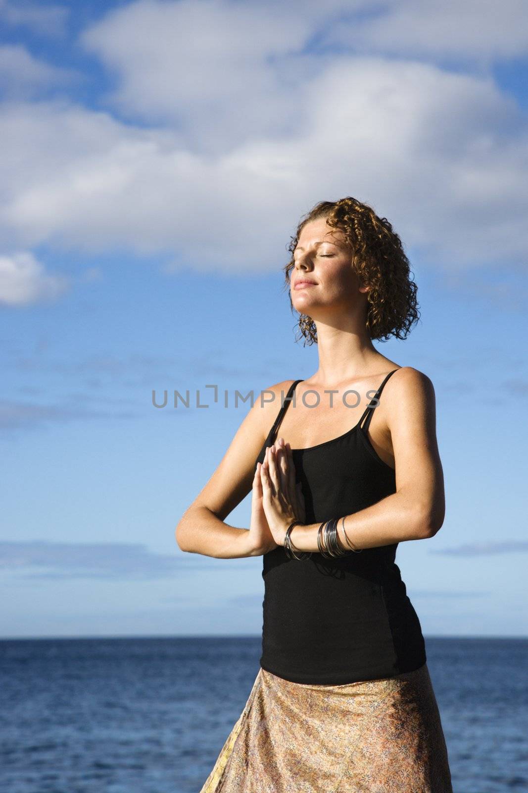 Woman meditating by ocean. by iofoto