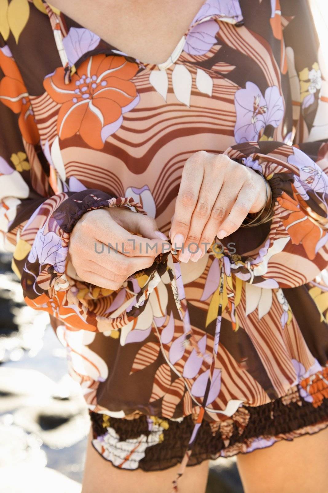 Close-up of woman's hands tying front of floral dress.