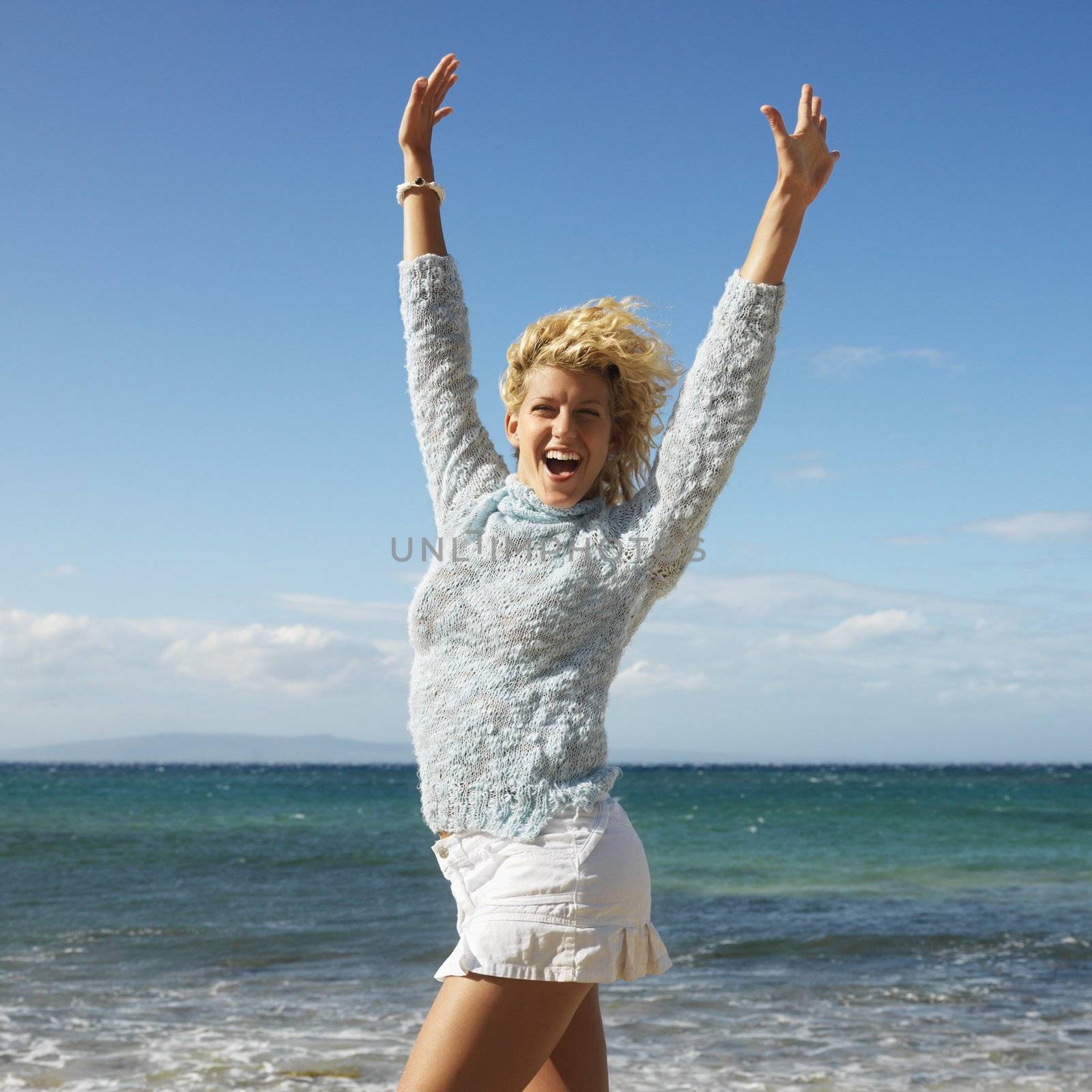 Portrait of attractive young blond woman smiling with arms raised in air on Maui, Hawaii beach.