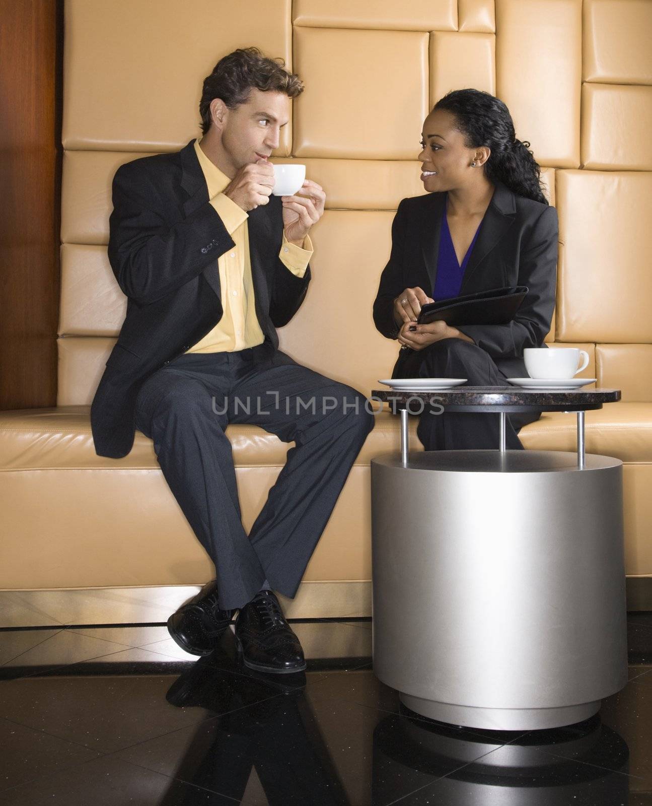 Caucasian businessman and African Amerian woman drinking coffee.