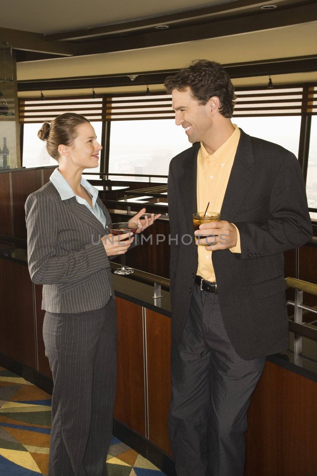 Caucasian business man and woman standing in bar with alcoholic beverages.