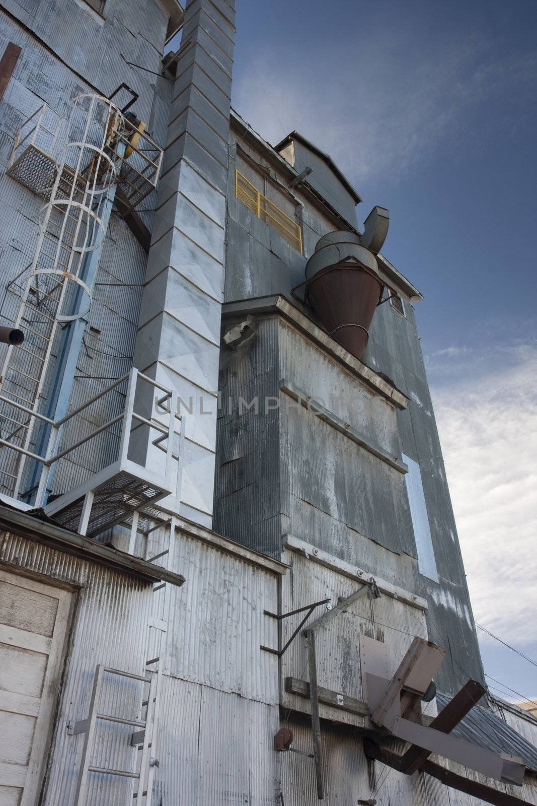 industrial background - a metal exterior of old grain elevator with pipes, ducts, ladders and chutes against sky