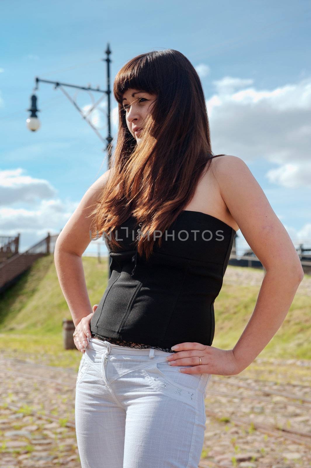 Young, beautiful woman stand with hands in line with the seam of the trousers.
