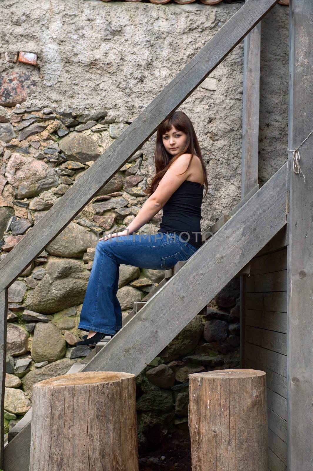 Young beautiful woman sitting on the stairs.
 near old castle ruins.