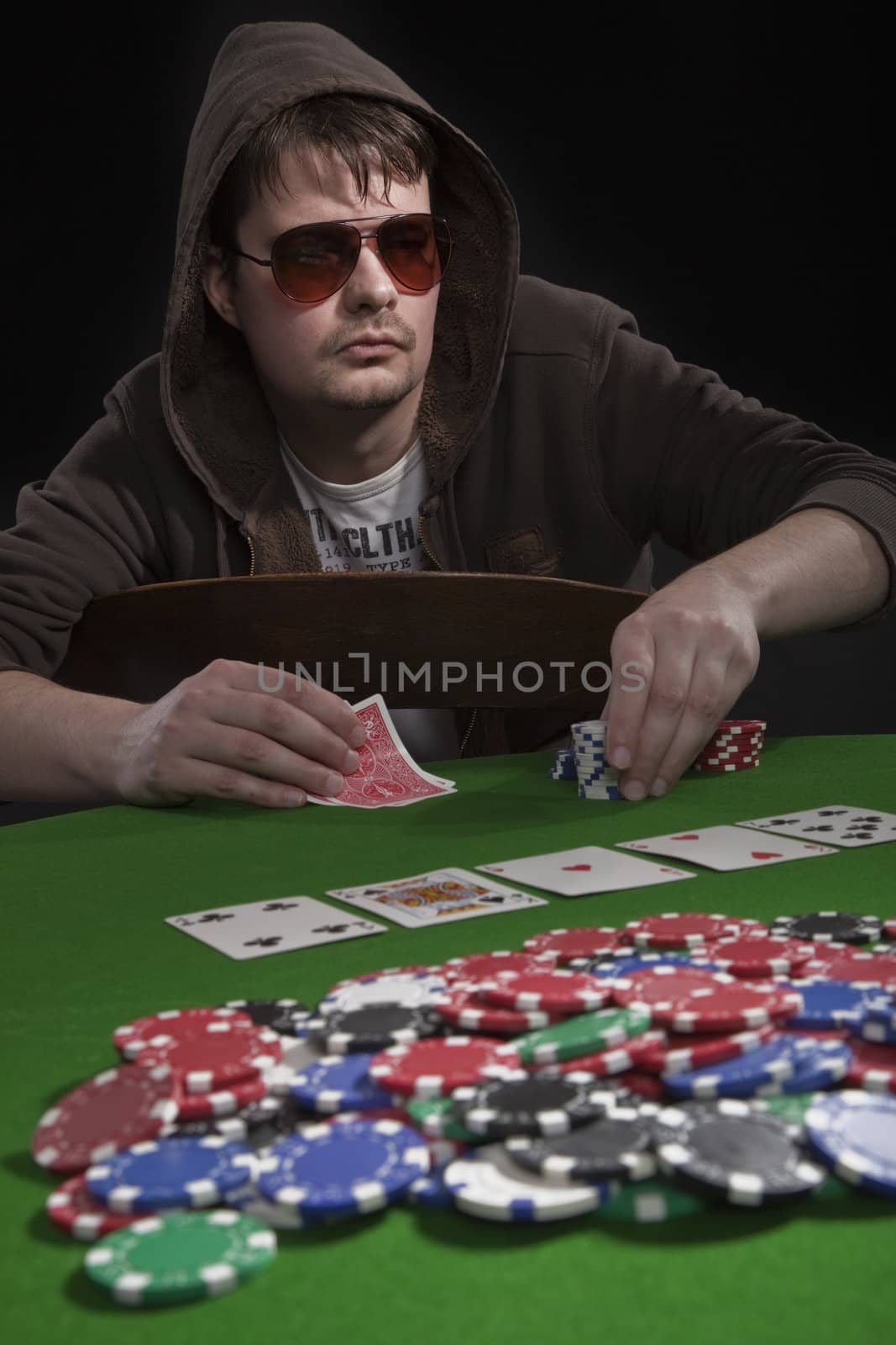 Man with sun glasses playing poker on green table. Chips and cards on the table.