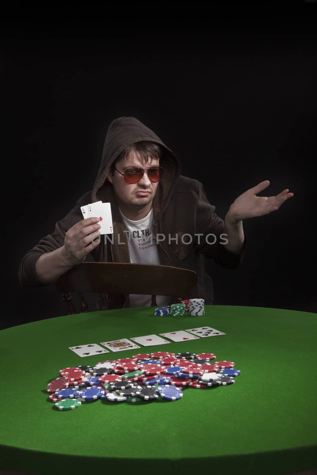 Man with sun glasses playing poker on green table. Chips and cards on the table.