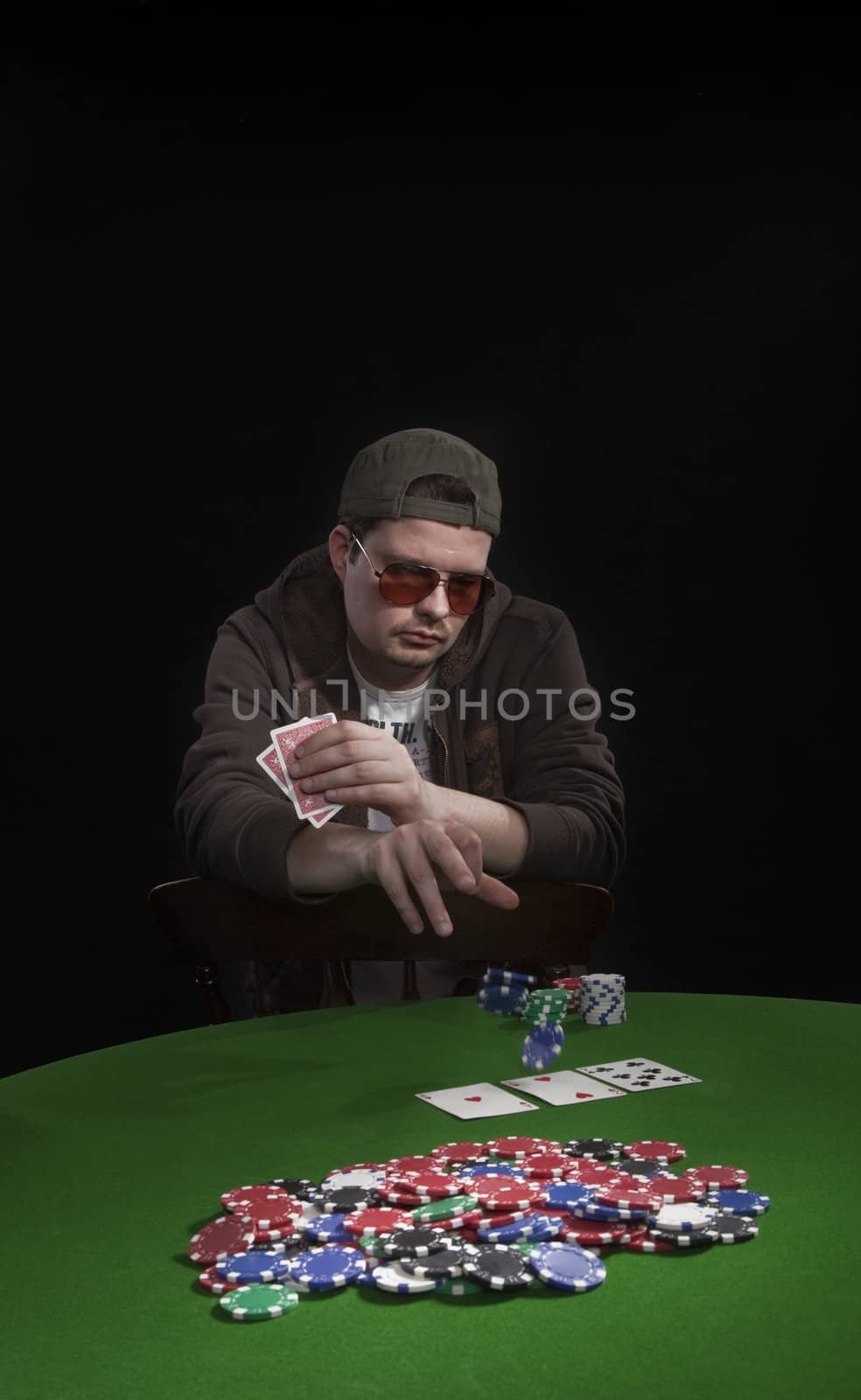 Man with sun glasses playing poker on green table. Chips and cards on the table.