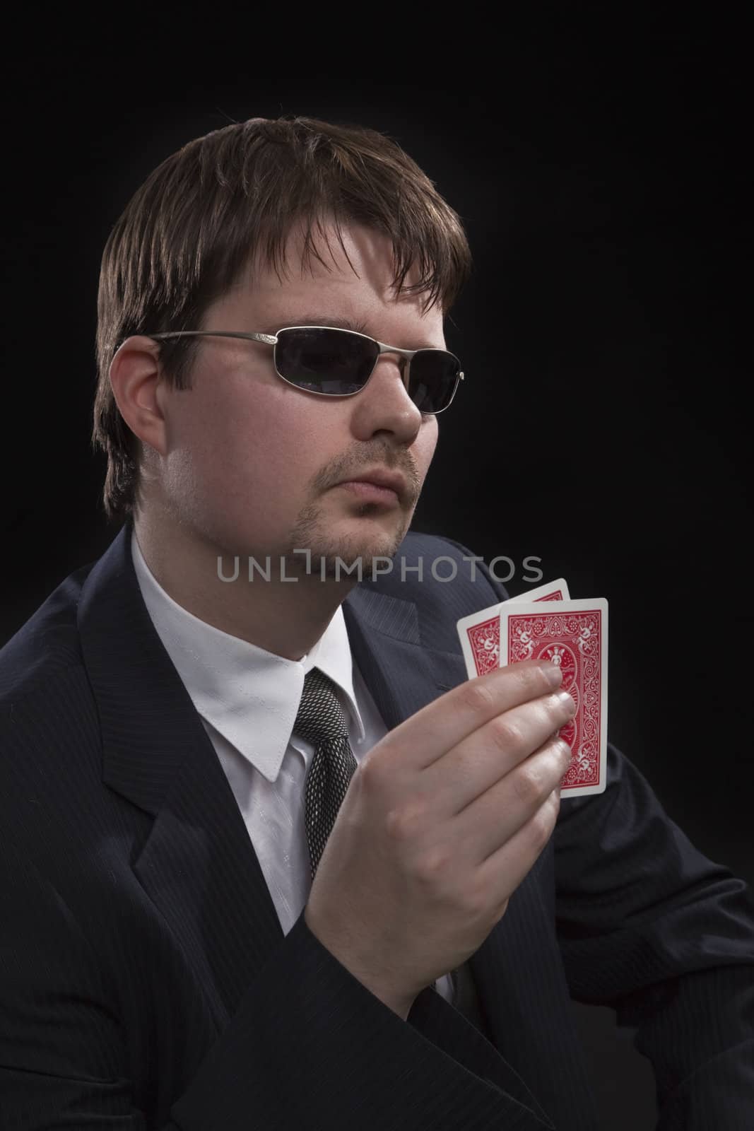 Man in suit with sun glasses playing poker on green table. Chips and cards on the table.