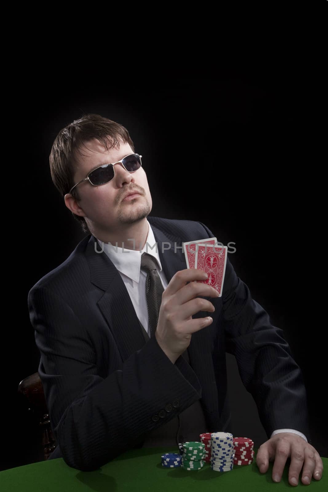 Man in suit with sun glasses playing poker on green table. Chips and cards on the table.