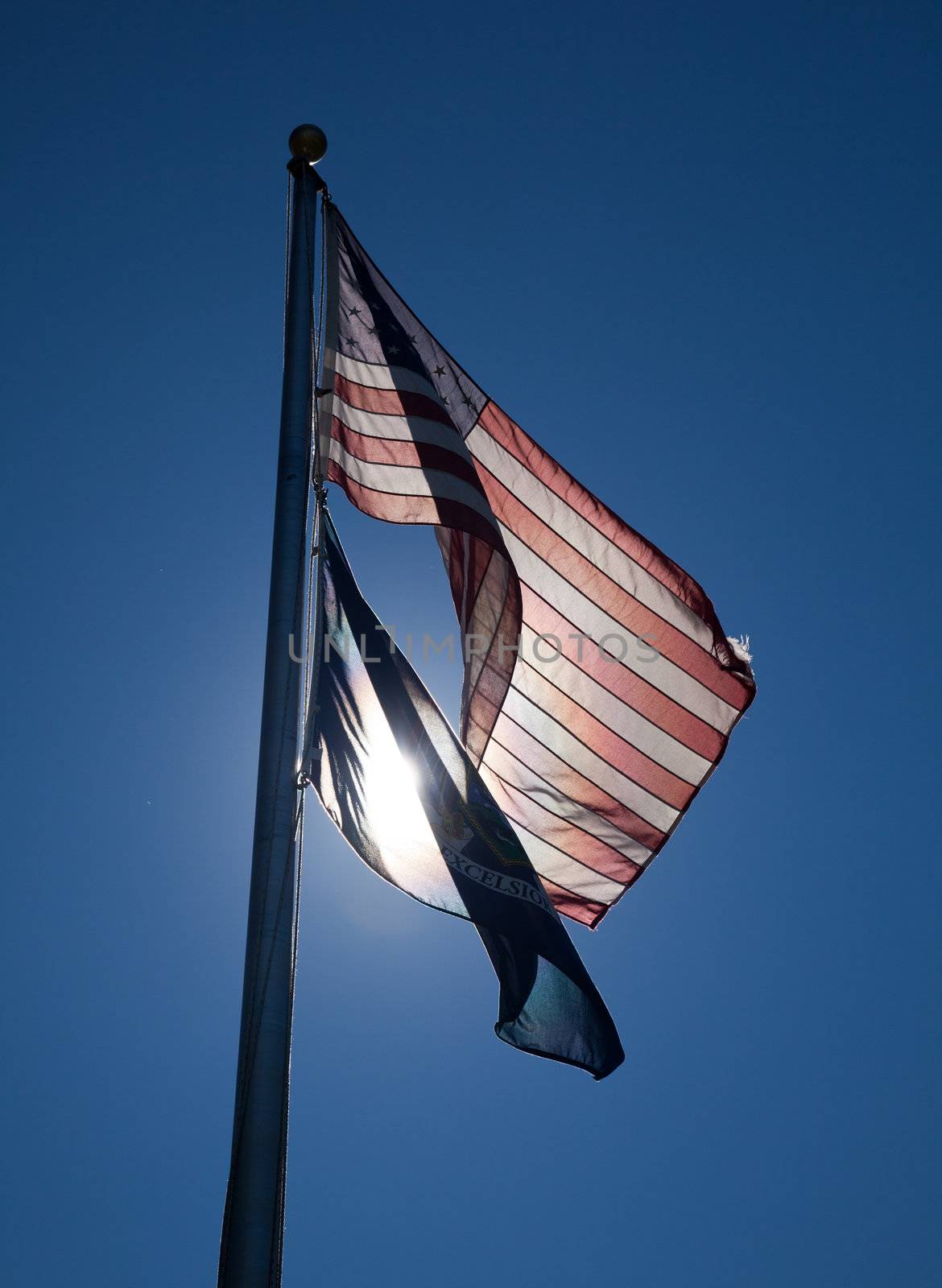 Stars and Stripes lit from behind and the New York State flag on a flagpole