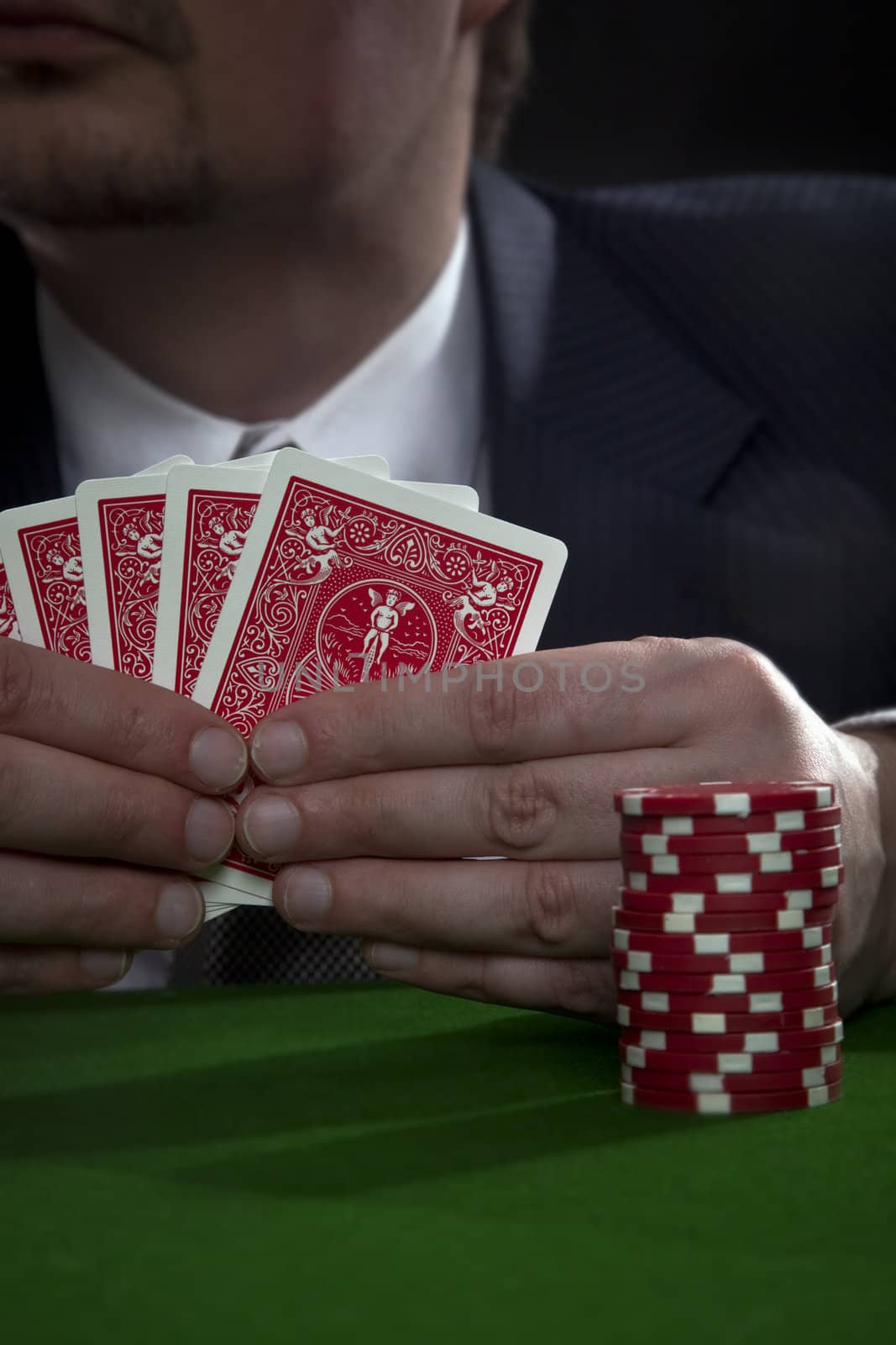 Man in suit with sun glasses playing poker on green table. Chips and cards on the table.