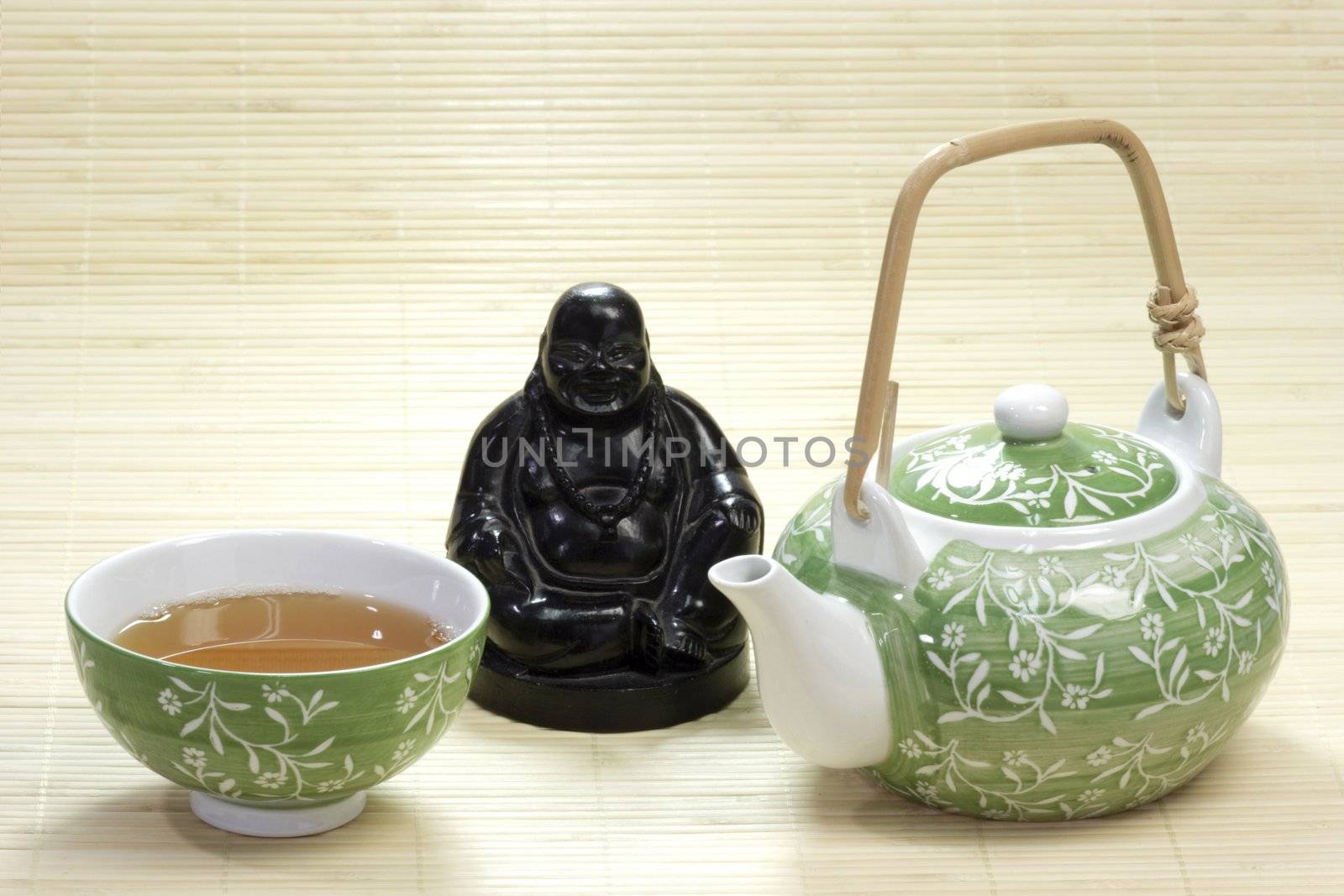 Green tea in a mug with teapot and buddha figure