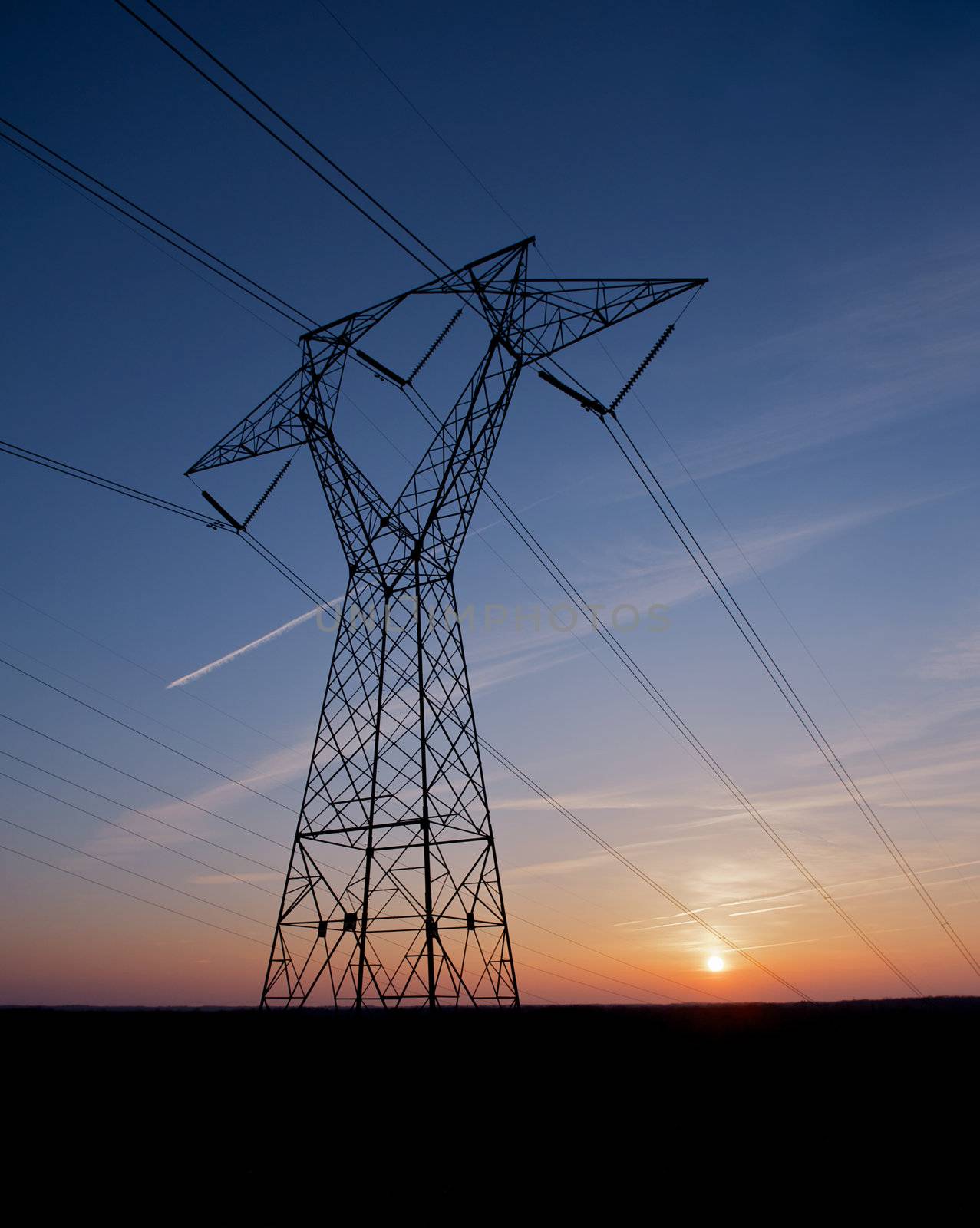 Electric power pylon and wires silhouetted by a colorful sunset. 
