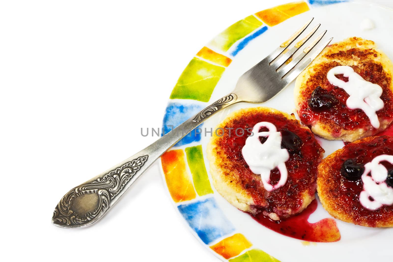 Cottage cheese pancakes with sour cream and blackcurrant jam on a colorful plate with fork