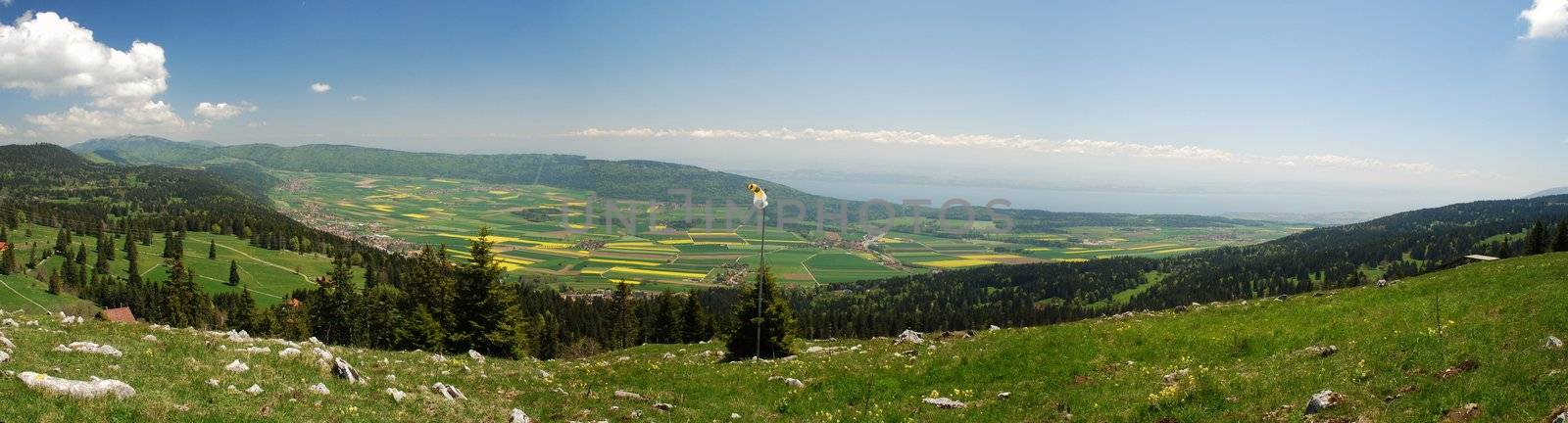 Panorama of Neuchatel region seen from Tete-de-Run hill, there is a weather-clock foreground, Jura woods coming down. In the plane of Ruz Valley there are yellow and green coloured fields, at right side we can see Neuchatel lake, just above there 