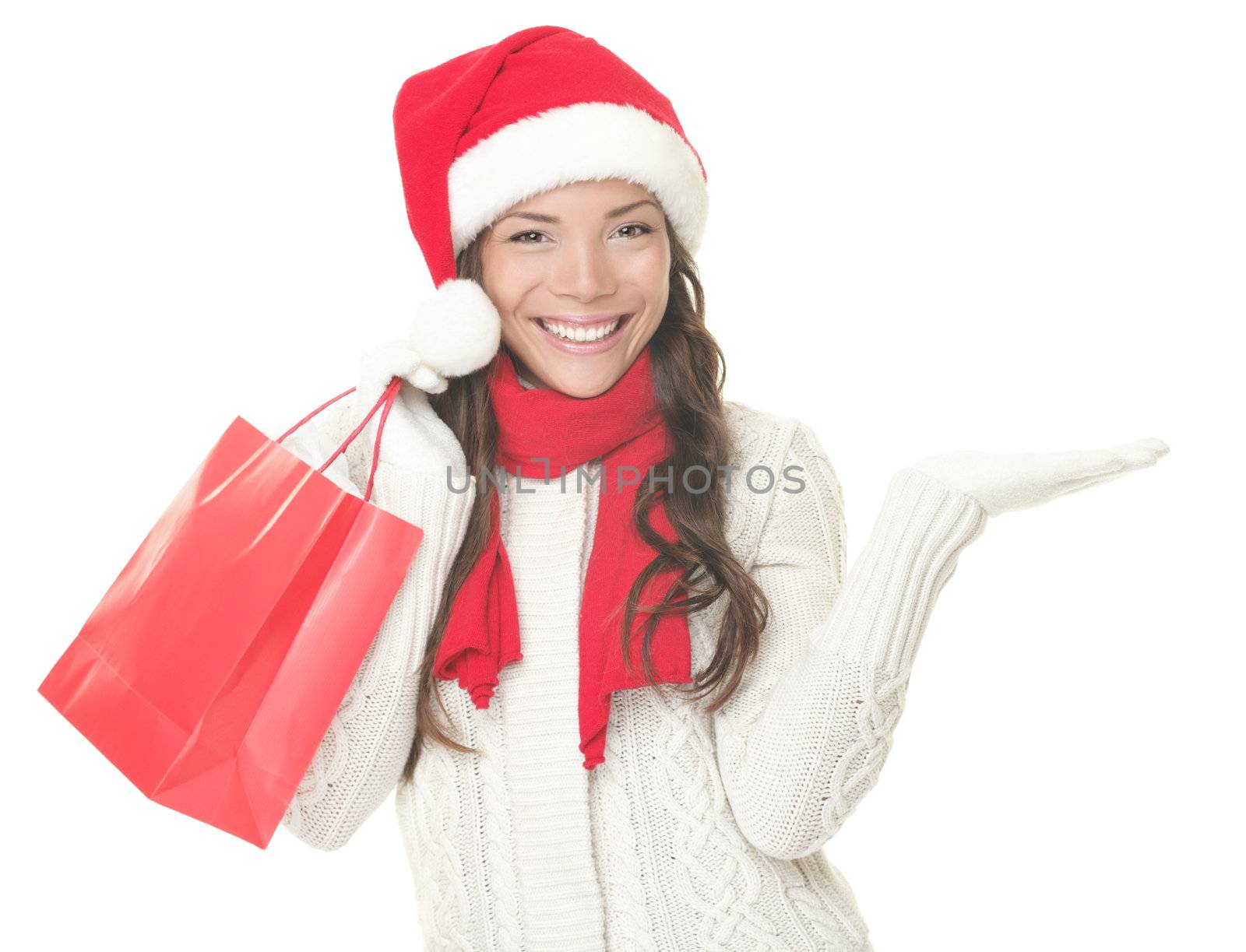 Christmas shopping woman presenting copy space. Excited santa girl showing your product or text looking sideways on copyspace with open hand palm. Closeup of mixed Asian Caucasian female model isolated on white background. 