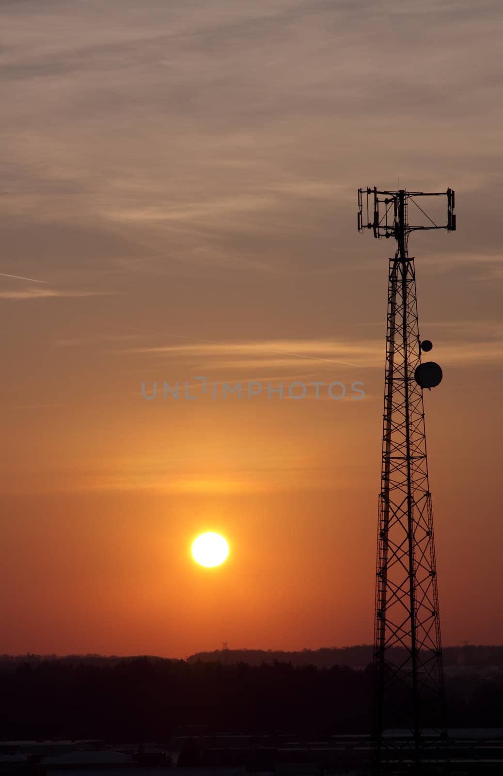 The silhouette of a cell phone tower shot against the orange cast of the setting sun.

