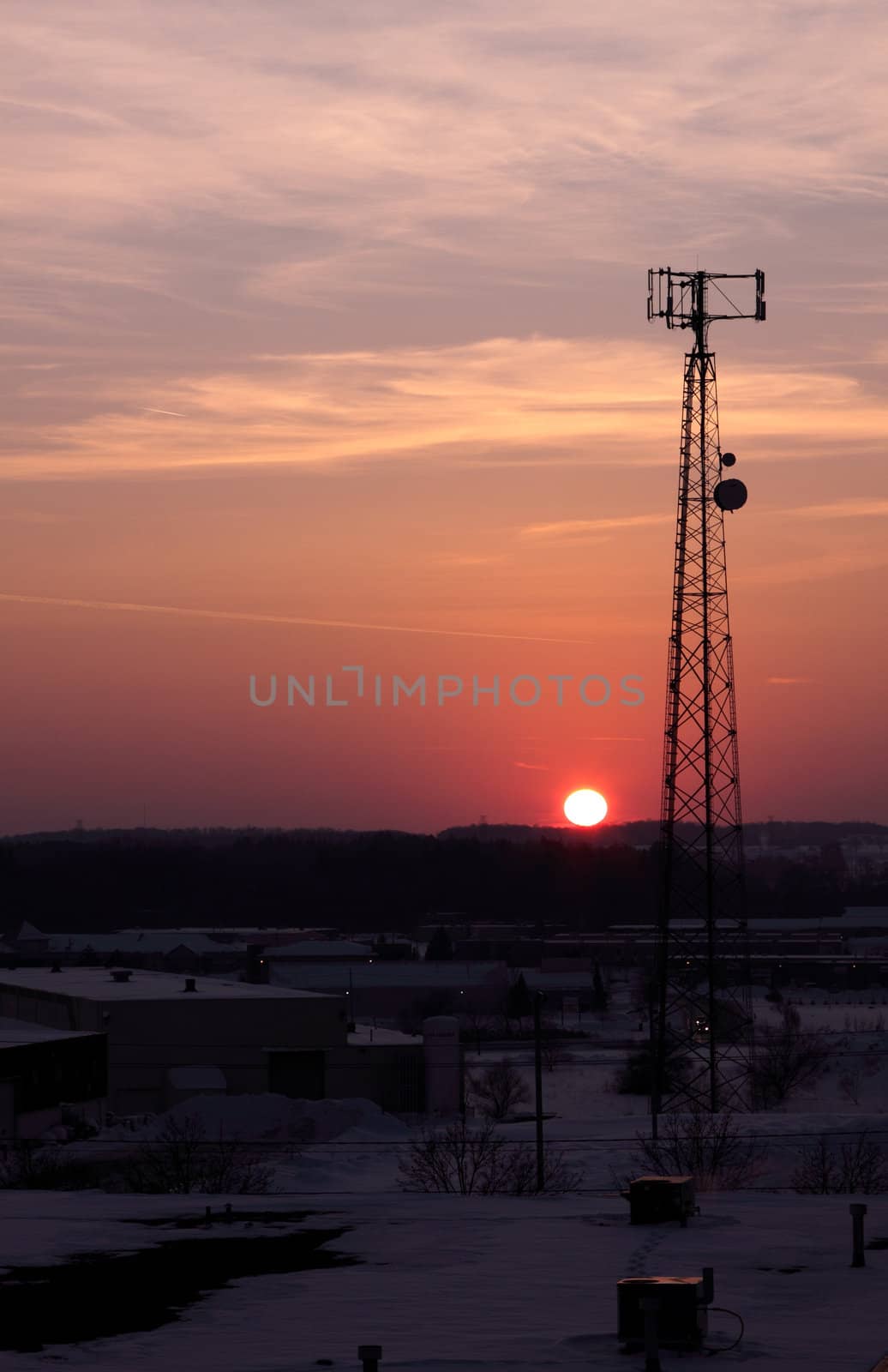 The silhouette of a cell phone tower shot against the orange cast of the setting sun.
