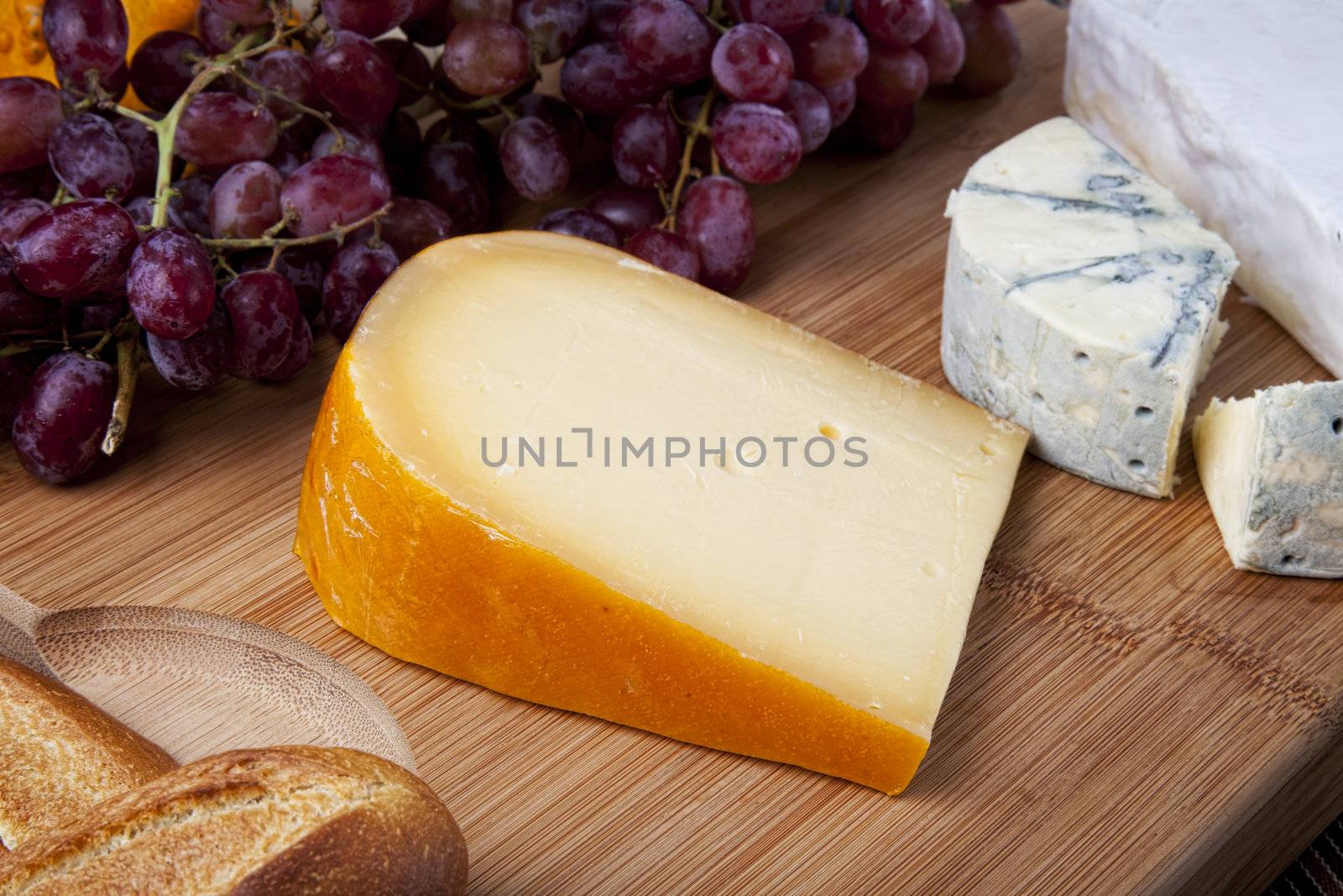 Fresh block of goude cheese, with blue cheese, grapes and bread.