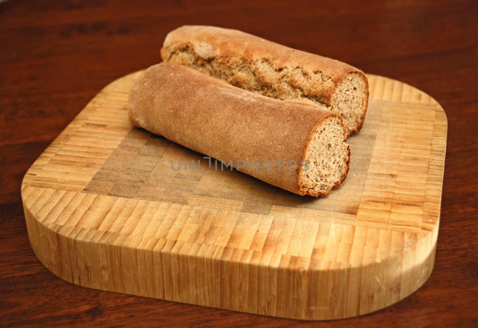 Homemade rye caraway bread cut in half on a wooden cutting board on a table.