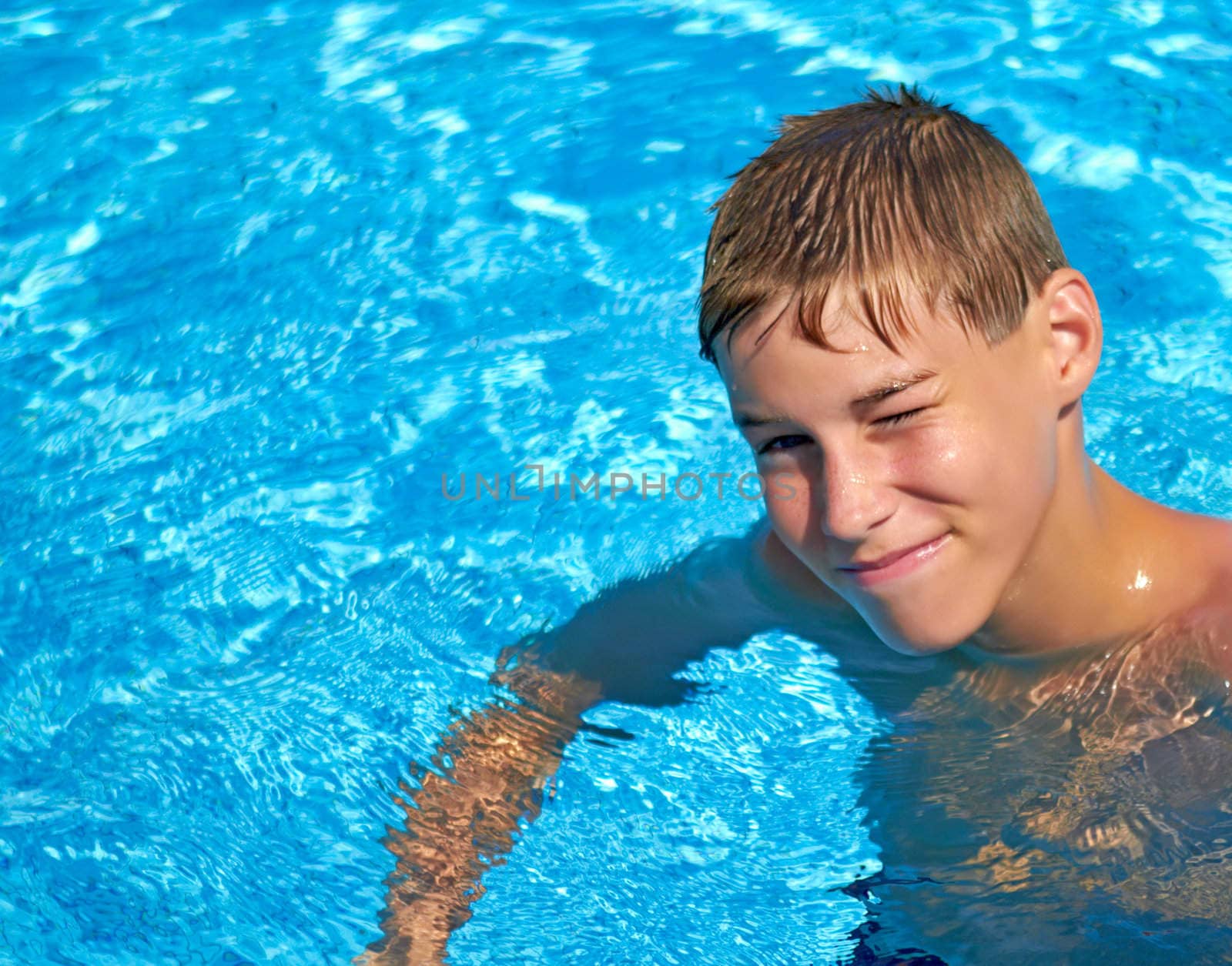 Smiling teenage boy having fun in the outdoor swimming pool.