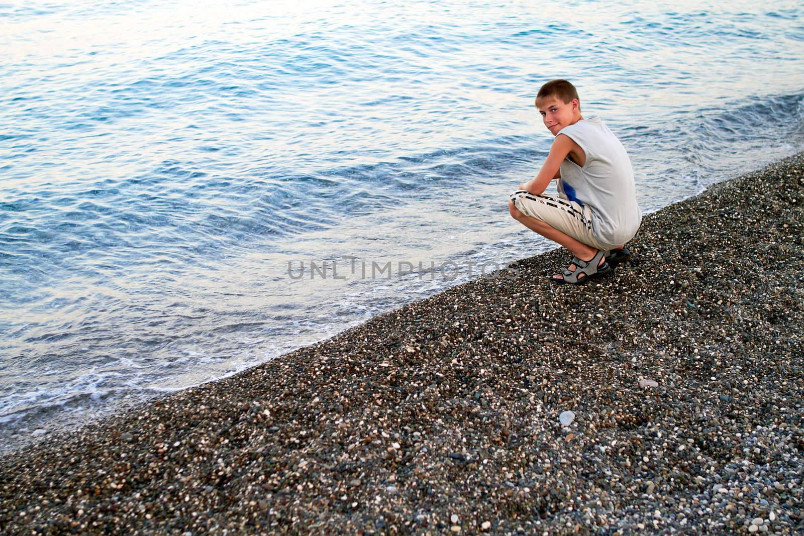 Smiling boy sitting at the evening pebble beach