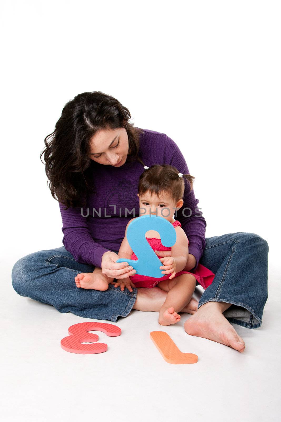 Mother, nanny, or teacher teaching baby to learn how to count one, two, three, with numbers in a playful way, while sitting on floor.