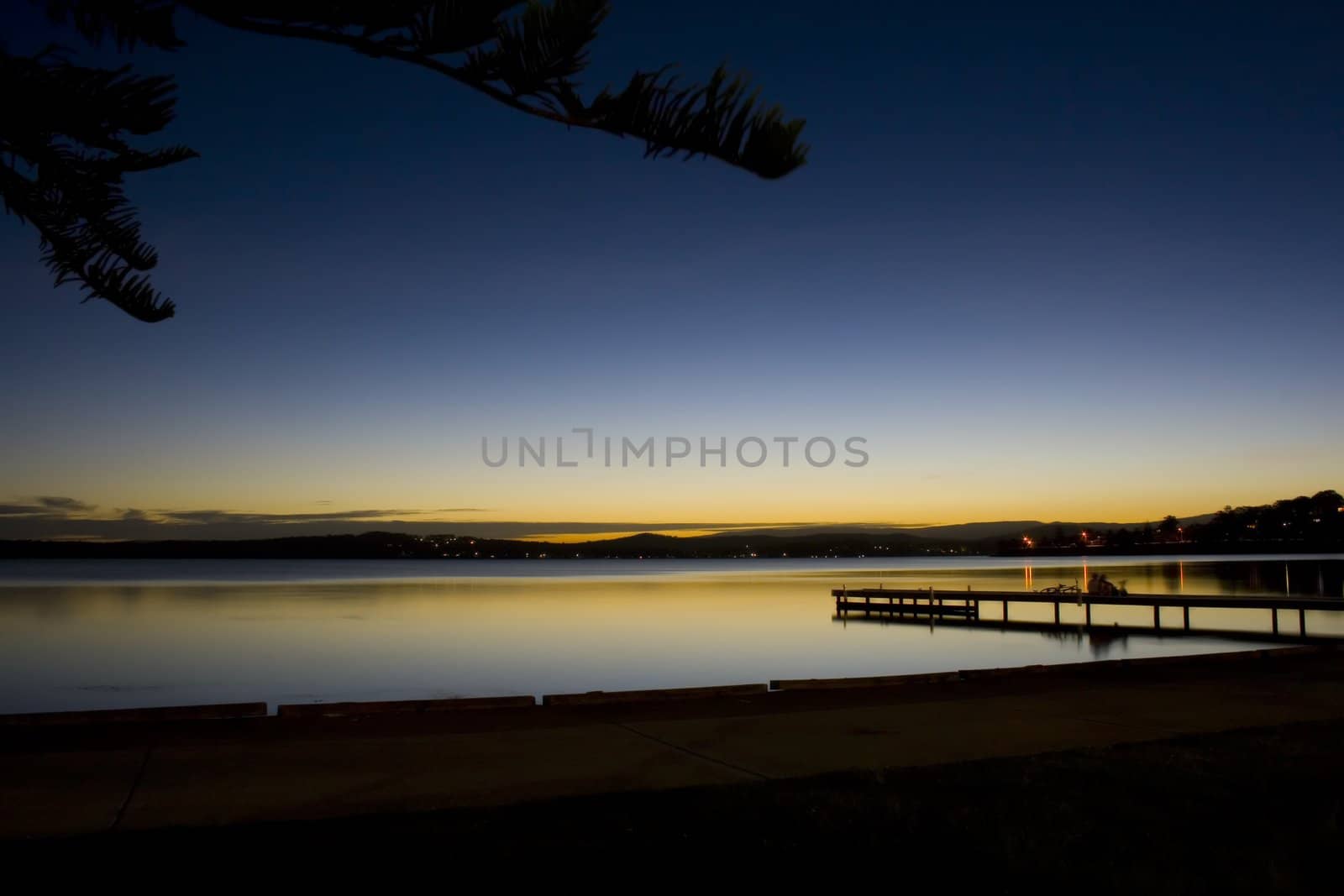 Peaceful long exposure overlooking calm water and a pier with children and bicycles.