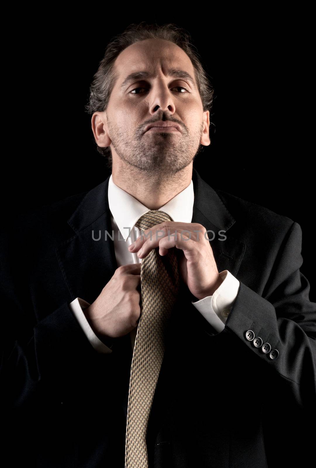 businessman tie fastening, overwhelmed expression on black background