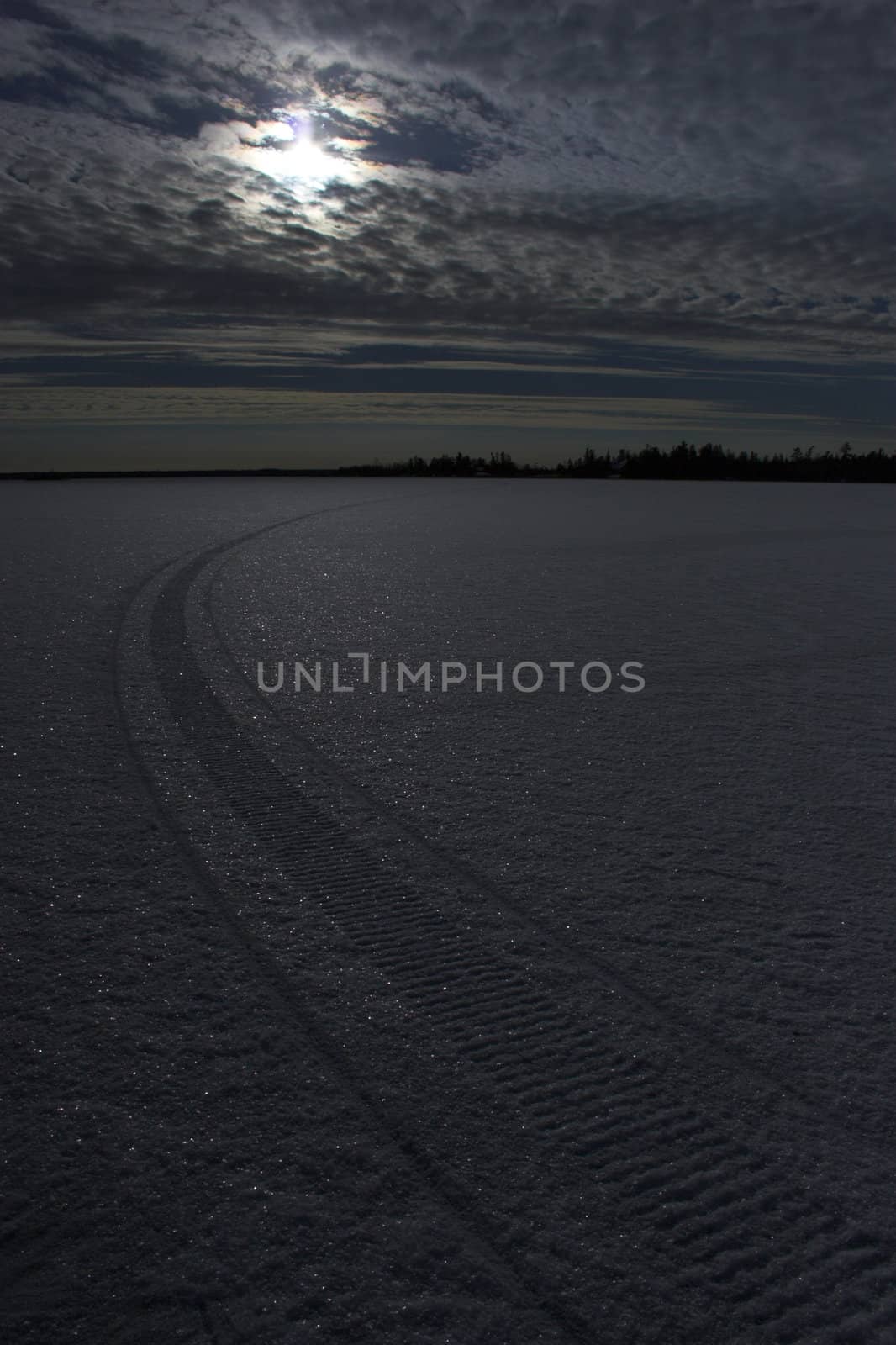 Snowmobile route at night over frozen lake with colorful reflections of the moon in snow crystals