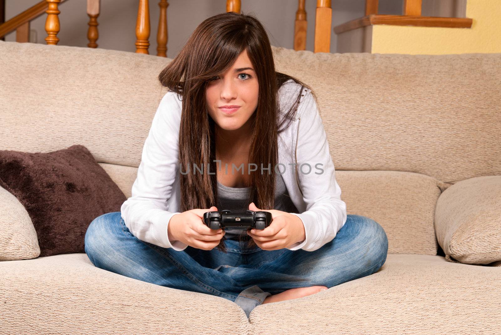 Young female concentrating playing videogames on sofa at home by dgmata