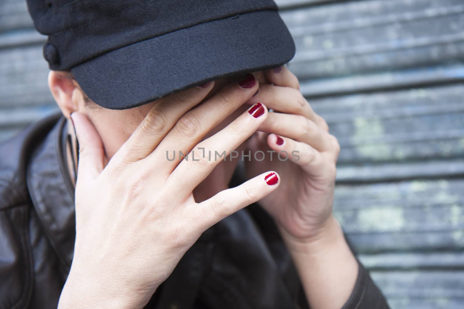 young woman wearing a cap, his face hidden in her hands