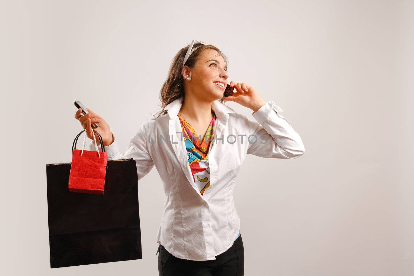 Modern looking young woman wearing white jacket talking on the phone and holding shopping bags
