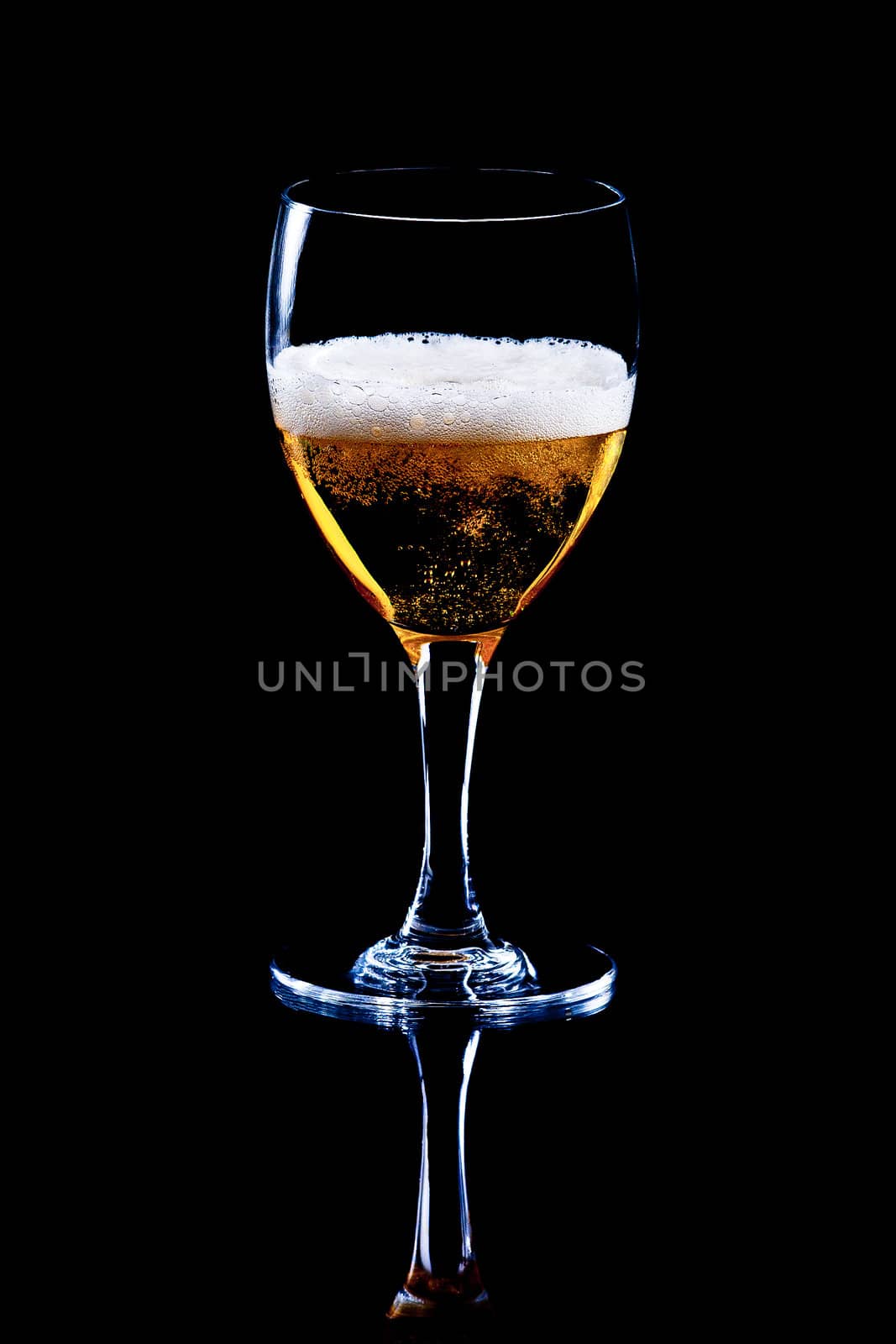 A glass with tasty beer on a black mirroring surface.