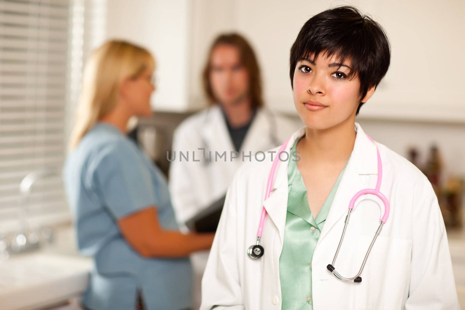 Pretty Latino Doctor Smiles at the Camera as Colleagues Talk Behind Her.