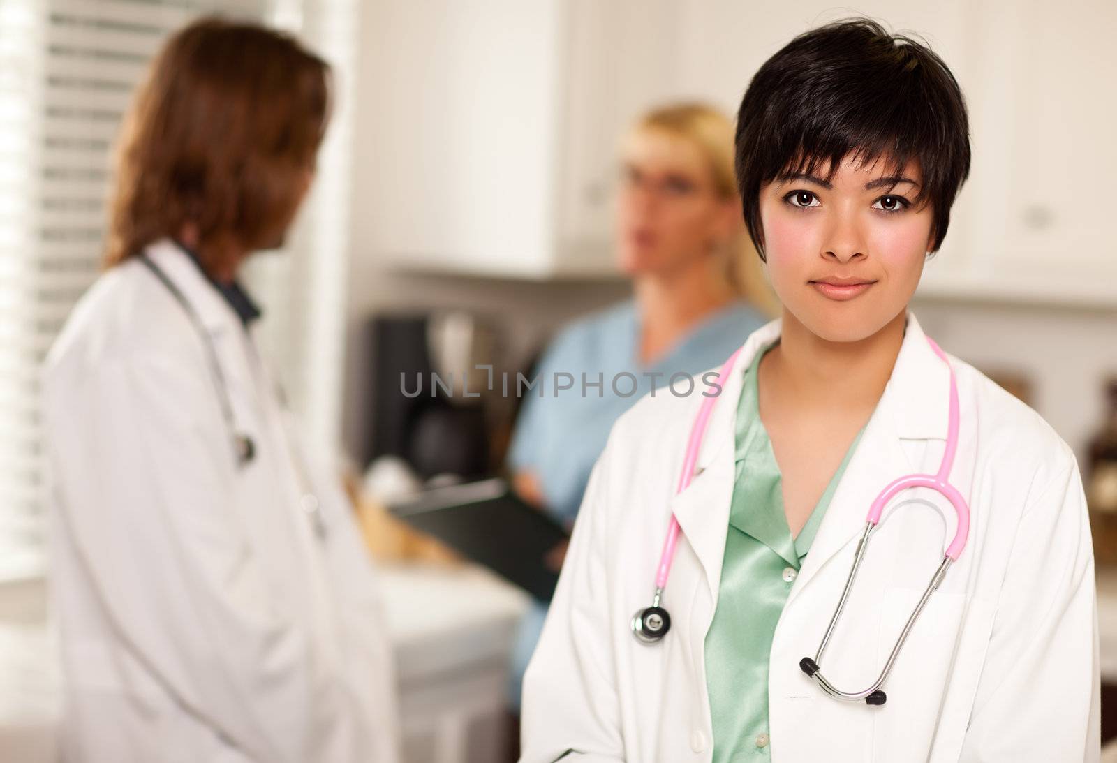 Pretty Latino Doctor Smiles at the Camera as Colleagues Talk Behind Her.