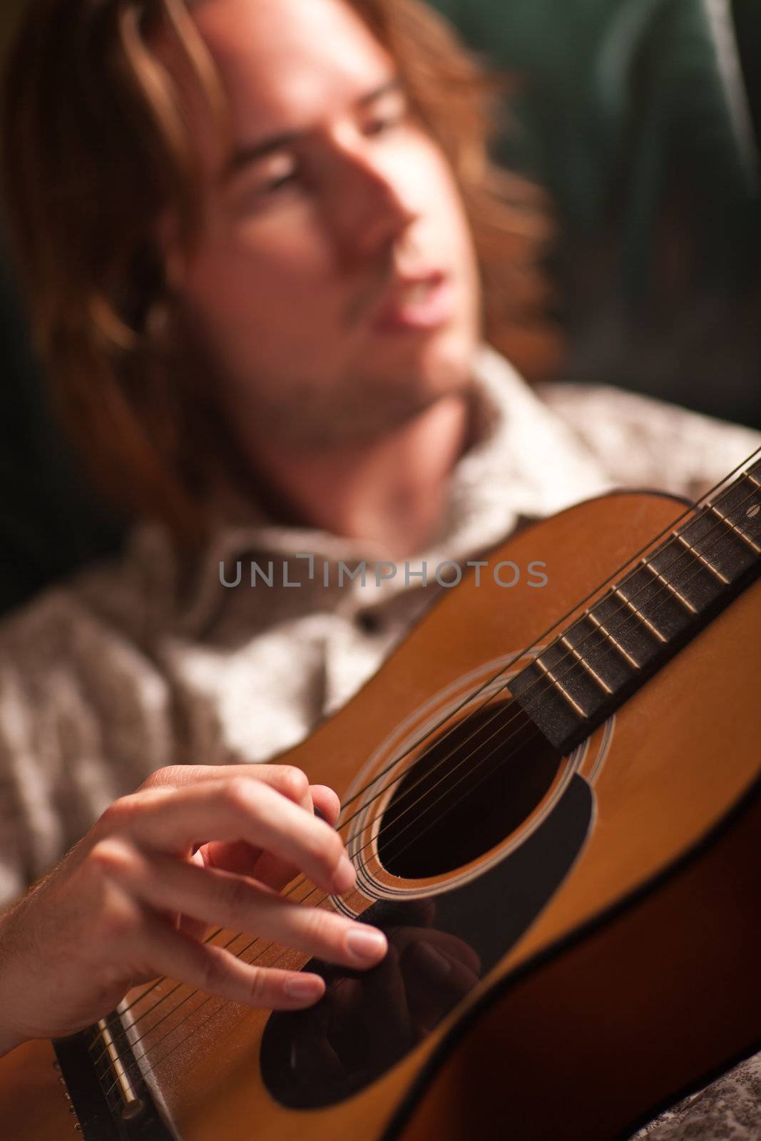 Young Musician Plays His Acoustic Guitar under Dramatic Lighting.