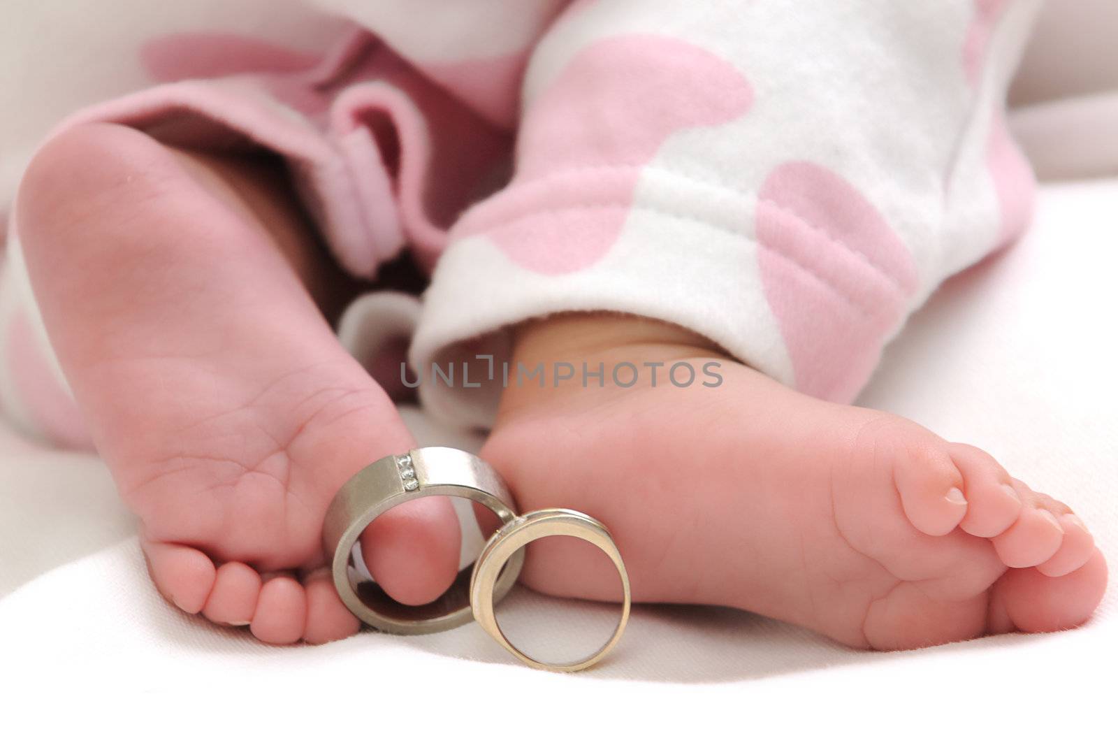 wedding rings on the toes of a baby girl wearing white and pink clothes
