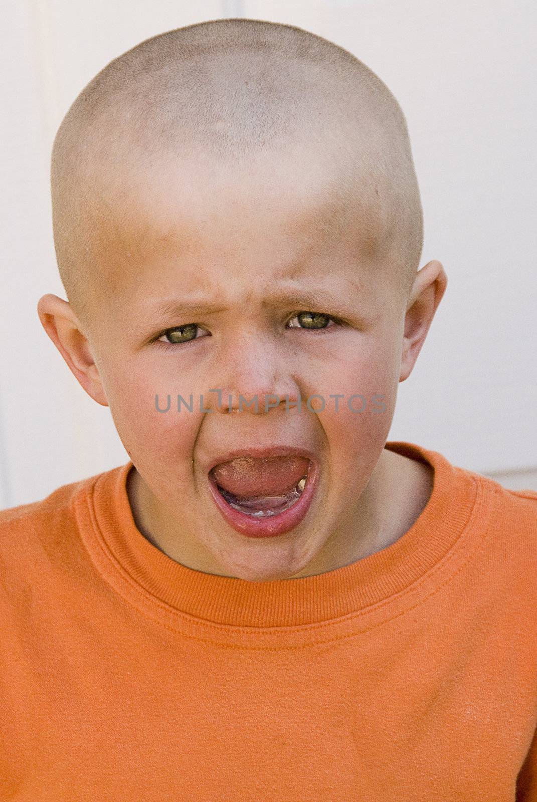 young frustrated boy with short hair, wearing orange shirt is screaming