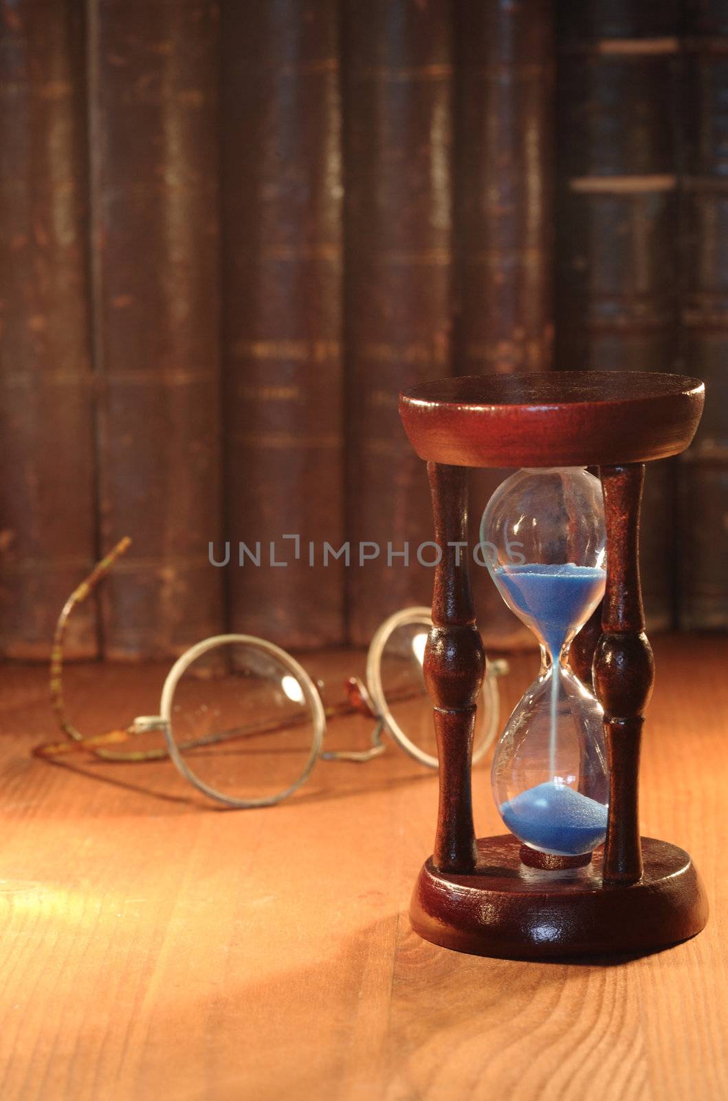 Vintage hourglass on background with old spectacles and books