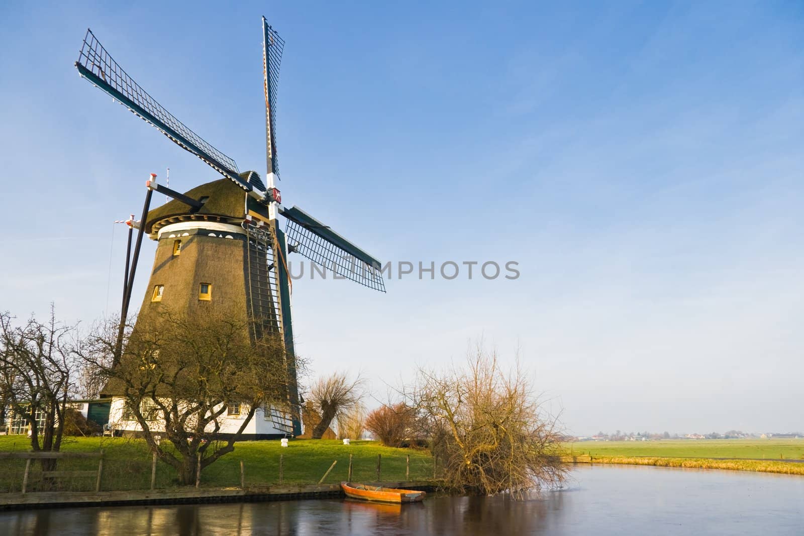 Dutch polder landscape with windmill  and boat on sunny winter day