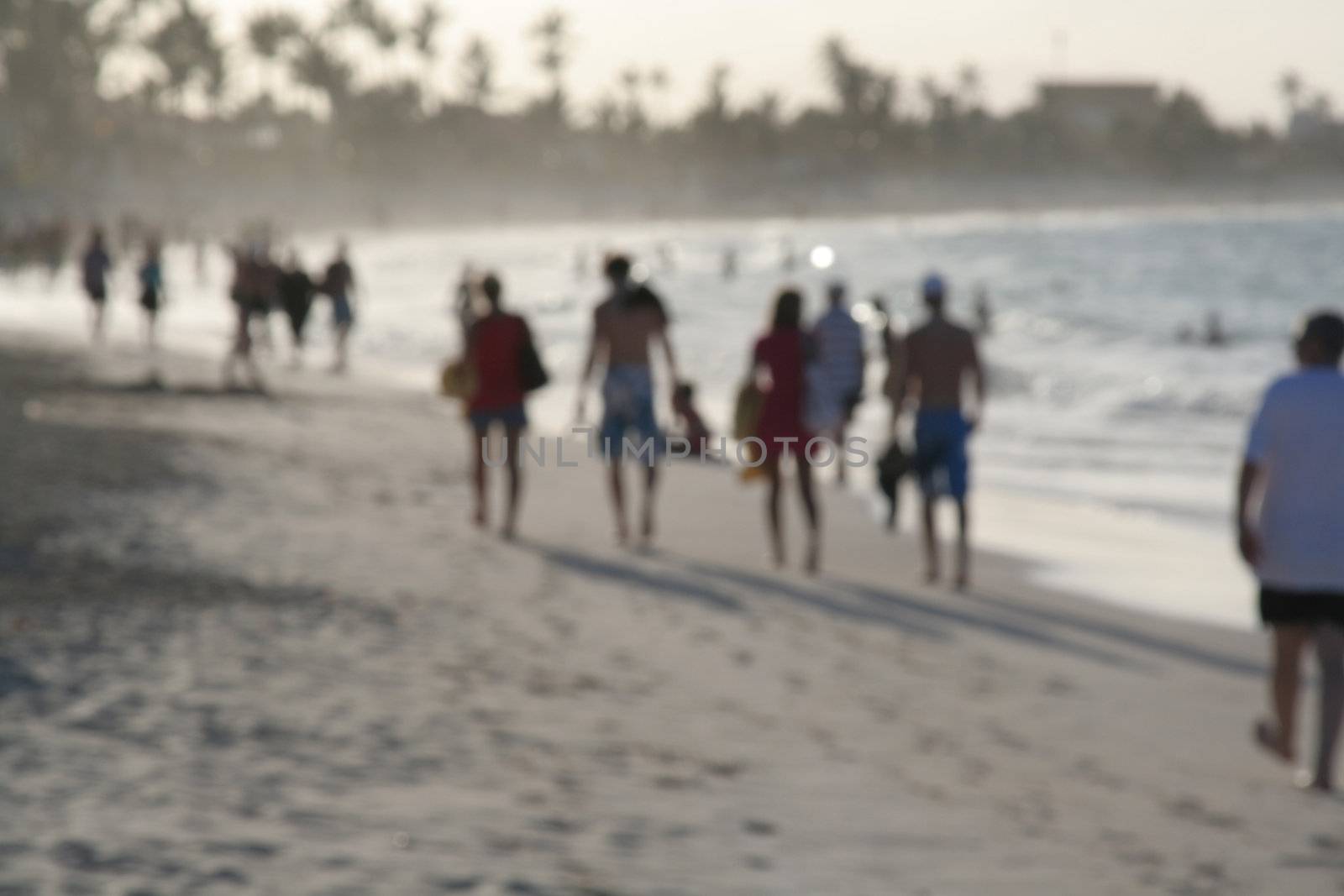 A blurred shot of a bunch of people walking on a tropical beach.