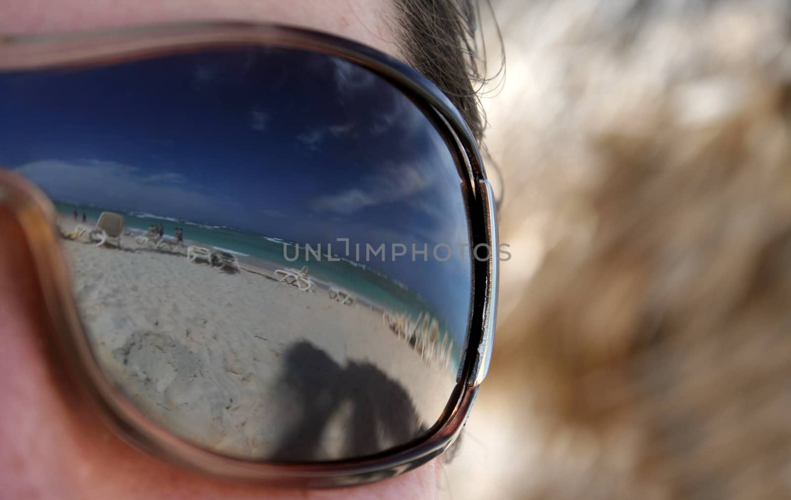 A closeup shot of a woman's sunglasses with the beautiful Punta Cana (Dominican Republic) beach in the reflection in them.
