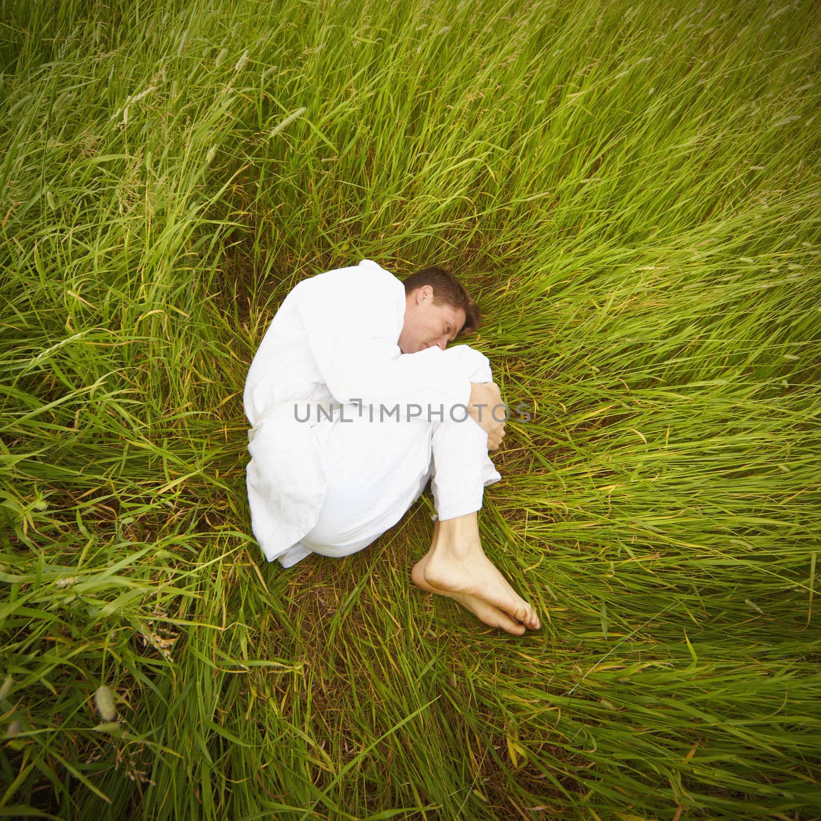 A man lying in the grass in the fetal position